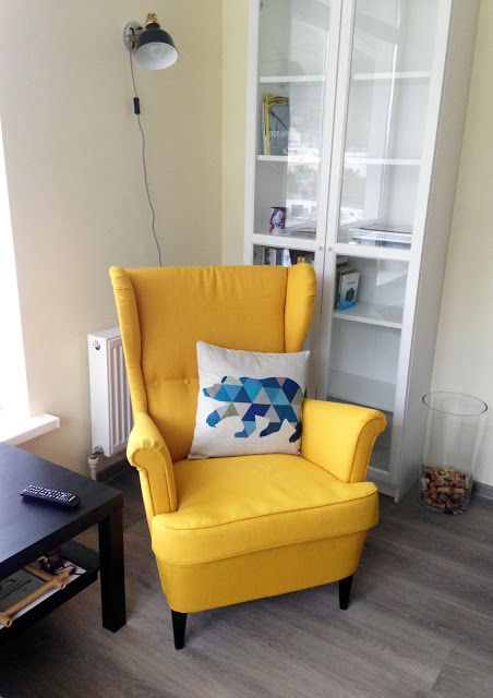 a small nook with a glass storage unit, a yellow Strandmon chair, a black coffee table and a printed pillow is a stylish space