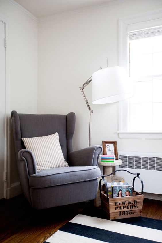 a small reading nook with a grey Strandmon chair, a striped rug, a wooden basket for storage and a side table