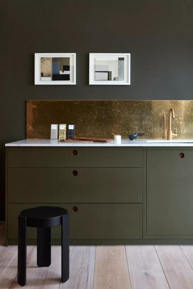 a sophisticated grey kitchen with sleek olive green lower cabinets, a polished gold backsplash and a black stool