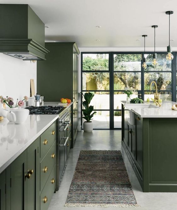 a stylish olive green kitchen with flat panel and shaker cabinets, white stone countertops and a backsplash, gold and brass knobs
