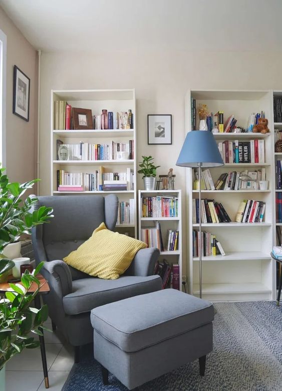 a stylish reading space with bookcases, a grey Strandmon chair and an ottoman, a blue floor lamp and some greenery