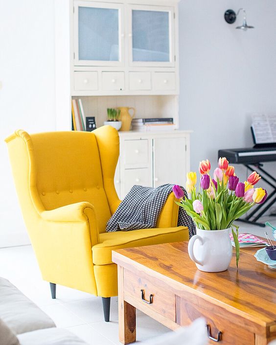 a yellow Standmon chair with a blanket, a stained coffee table and bold tulips in a jar make the space look bold and cool