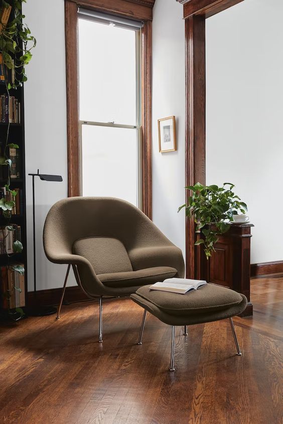 an elegant nook with stained frames and furniture, a brown Wumb chair and ottoman and some greenery