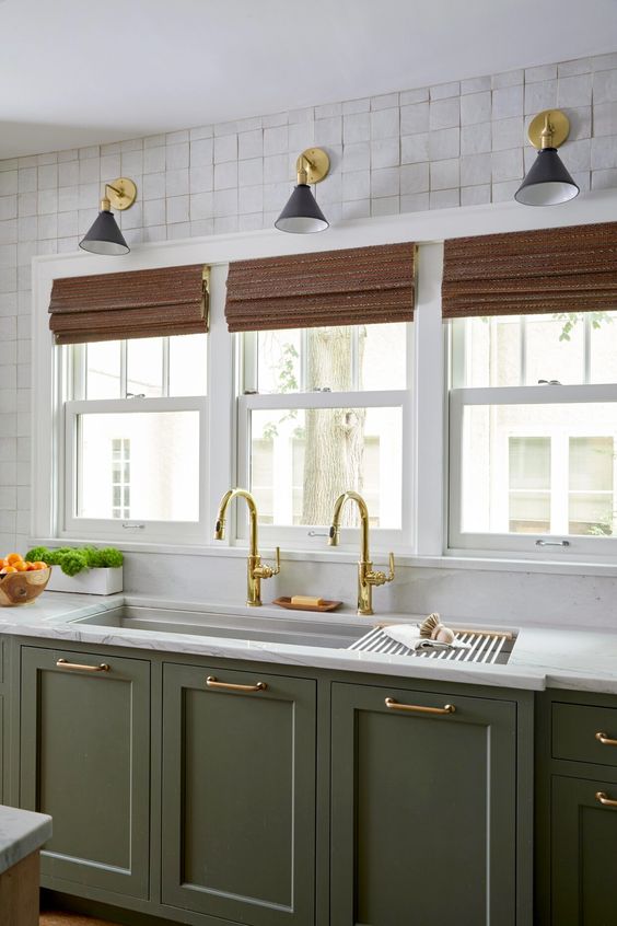 an olive green farmhouse kitchen with lower cabinets, white stone countertops, woven shades and black and gold sconces