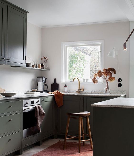 an olive green kitchen with flat panel and shaker cabinets, white stone countertops, open shelves and a wooden stool