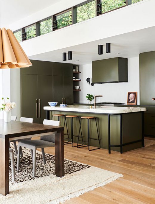 an olive green kitchen with flat panel cabinets, a large kitchen island, white and black countertops, black touches and lamps