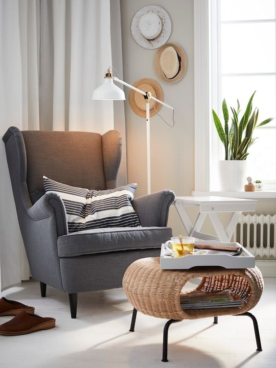 grey Strandmon wing chair by IKEA styled with a striped pillow and with a woven round ottoman is a cool idea for many spaces