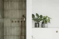 02 a chic modern bathroom with a shower space clad with olive green skinny tiles, a white space with a toilet and potted plants