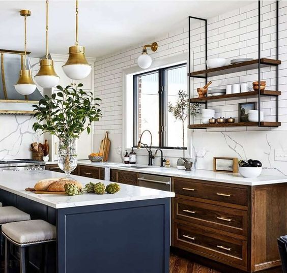 a chic modern kitchen with stained cabinets, a navy kitchen island, white countertops and a backsplash, suspended shelves and brass pendant lamps
