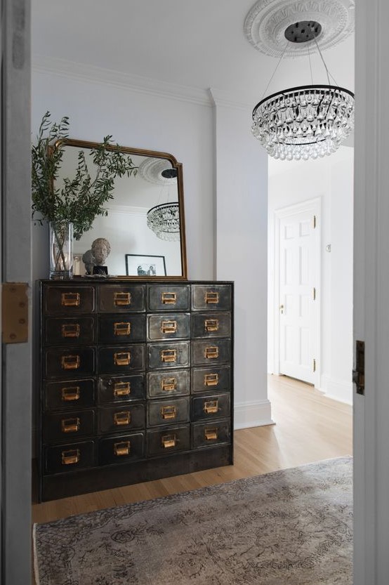 a dark-stained shabby chic card cabinet, a mirror and greenery on it adds vintage chic to the entryway and makes it refined