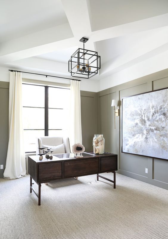 a farmhouse home office with olive green paneling, a dark-stained desk and a creamy chair, a geometric pendant lamp