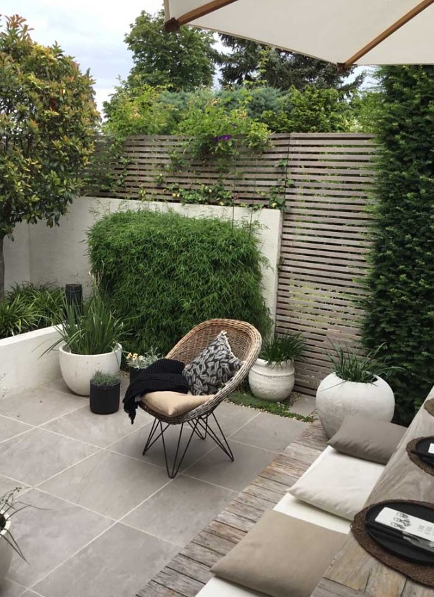 a contemporary walled backyard with a planked screen, with a tiled floor, potted grasses and greenery, a small dining set with pillows and a woven chair a contemporary walled backyard with a planked screen, with a tiled floor, potted grasses and greenery, a small dining set with pillows and a woven chair