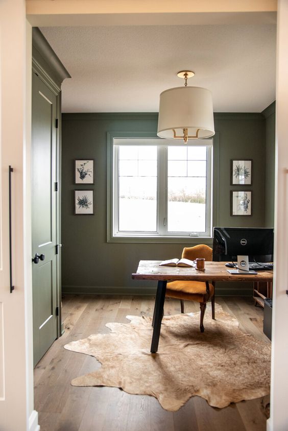 a farmhouse olive green home office with a wooden desk and a marigold chair, a pendant lamp and some artwork
