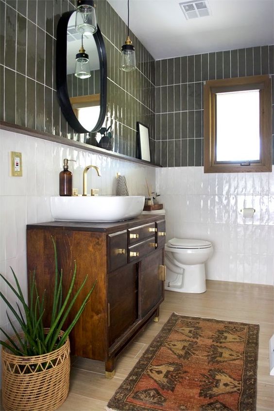 a mid century modern bathroom with olive green and white skinny tiles, a dark stained vanity, an oval mirror and a potted plant