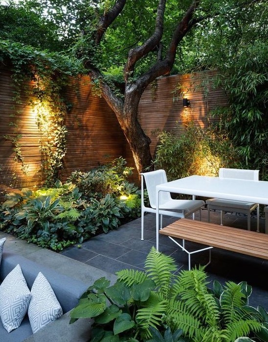 a contemporary townhouse garden with stone tiles, minimalist furniture of wood and metal, lush textural greenery and a tree growing a contemporary townhouse garden with stone tiles, minimalist furniture of wood and metal, lush textural greenery and a tree growing