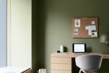 11 a minimalist olive green home office with a windowsill daybed, a stained desk and a grey chair, a cork board and a lamp