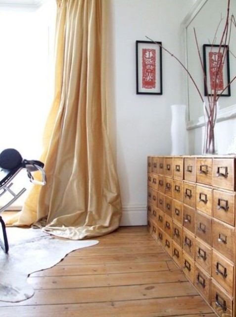 a lovely light-filled space with elegant tan curtains, a light-stained card cabinet, a large mirror and some decor is beautiful