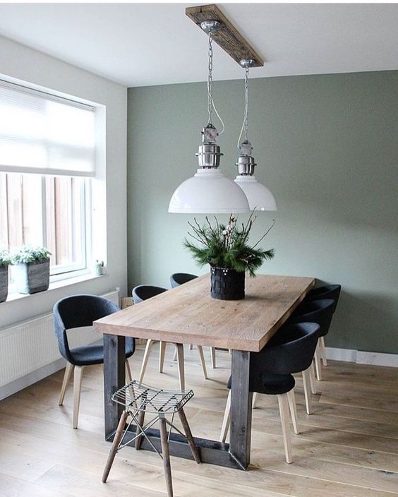 a modern farmhouse dining room with an olive green accent wall, a stained wood dining table, black chairs, white pendant lamp
