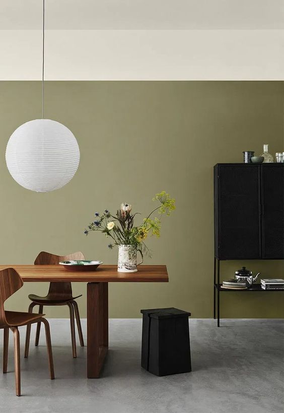 a refined olive green dining room with a stained table and plywood chairs, a black storage unit and a pendant lamp