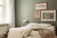 17 a relaxing bedroom with olive green walls, a bed with neutral layered bedding, a woven bench, a crystal chandelier and some art