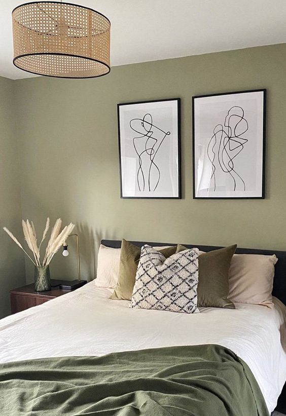 a Scandinavian bedroom with olive green walls, a dark green upholstered bed with printed and neutral bedding, a mini gallery wall and a woven pendant lamp