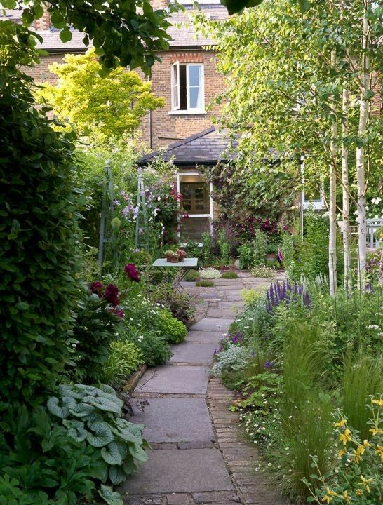 a cute narrow garden with a tile pathway, greenery and blooms is a dreamy space with a dining set a cute narrow garden with a tile pathway, greenery and blooms is a dreamy space with a dining set