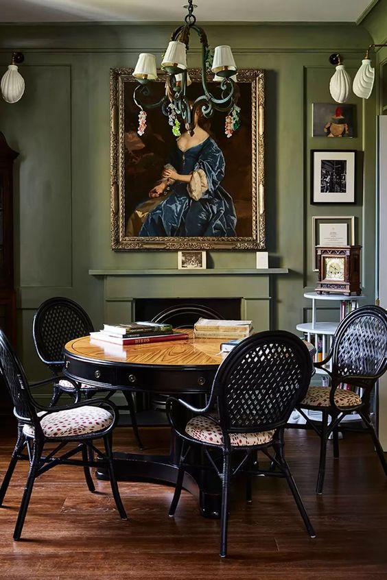 a sophisticated dining room with olive green walls, a fireplace, a stained table, black chairs, refined lamps and artwork