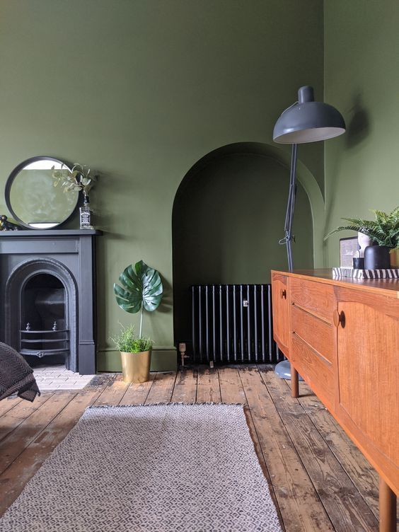 a vintage olive green living room with a non working fireplace, a niche with a credenza, a stained sideboard, a grey floor lamp and a mirror