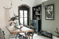 an eclectic dining room with an olive green accent wall, a stained table and metal and wood chairs, hanging bulbs, a built-in sideboard