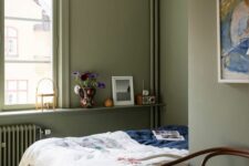 27 an olive green bedroom with a bed and colored bedding, a paper pendant lamp and a windowsill with decor