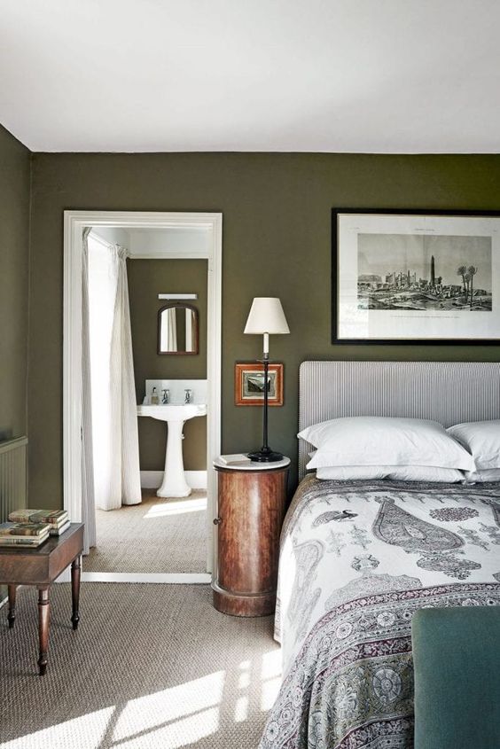 an olive green bedroom with a printed upholstered bed and bedding, a black and white artwork, stained furniture