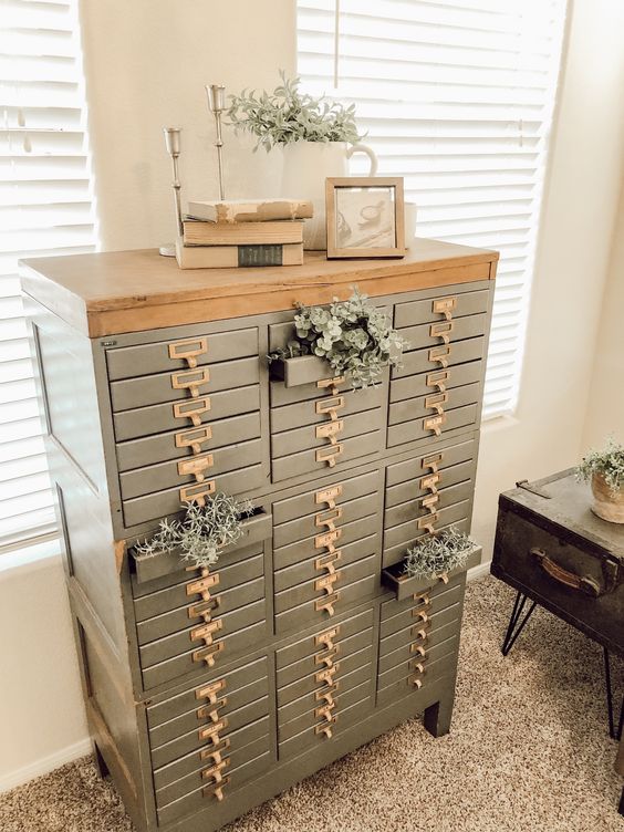 a grey file cabinet styled with air plants, books, art and some candleholders is a cool addition to a vintage space