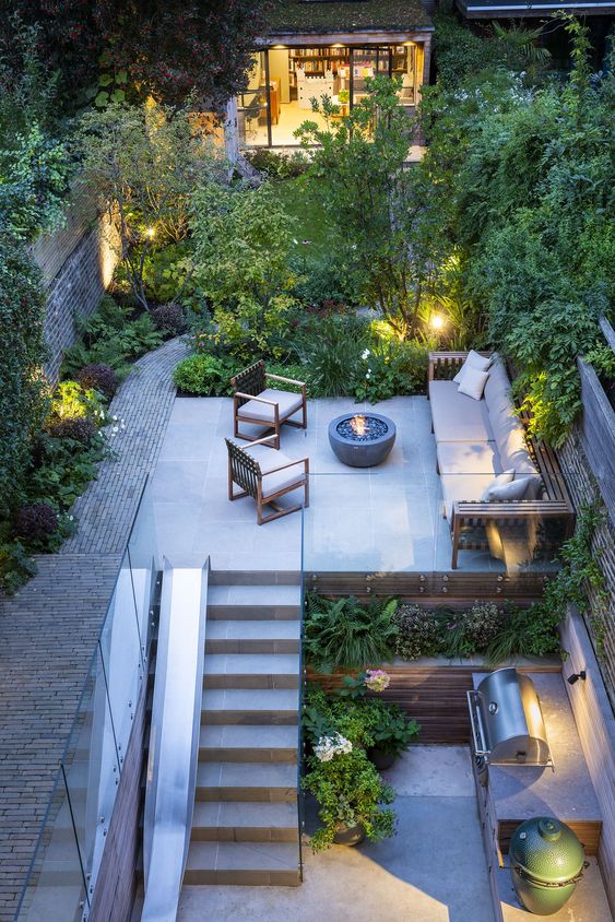 a cool garden with several levels, with greenery and treesm lights and garden furniture plus a bbq zone in the lower level a cool garden with several levels, with greenery and treesm lights and garden furniture plus a bbq zone in the lower level