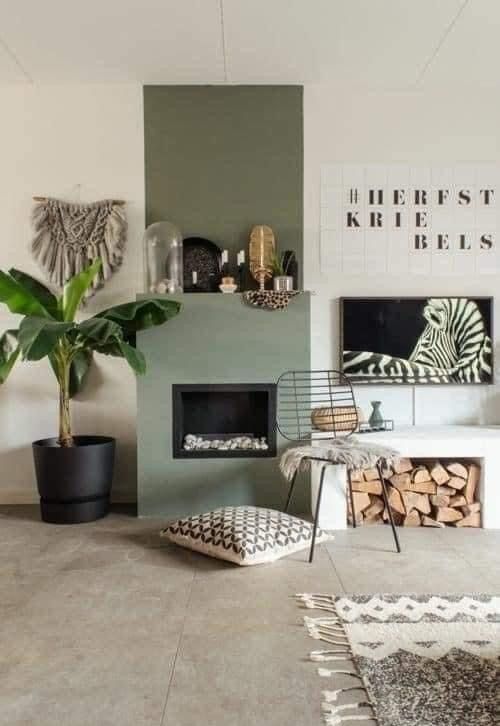 a cool boho nook with an olive green fireplace, a bench with firewood storage, some art and a potted plant