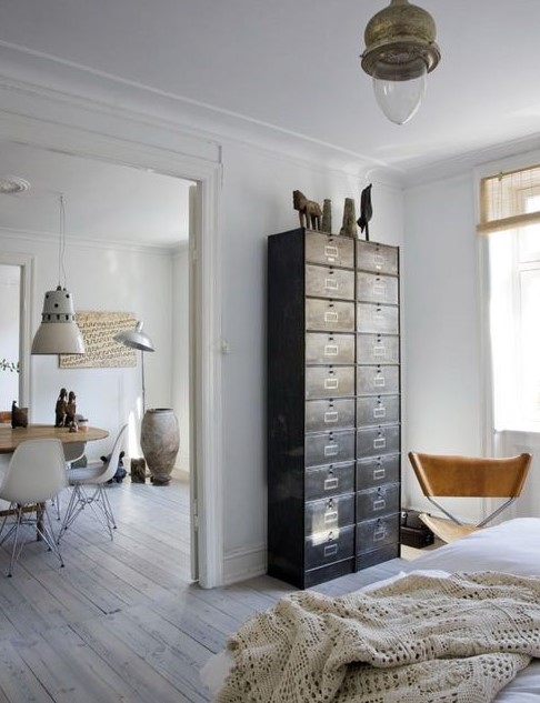 a light-filled Scandinavian space with a dark card cabinet that is used instead of a usual dresser and a leather chair