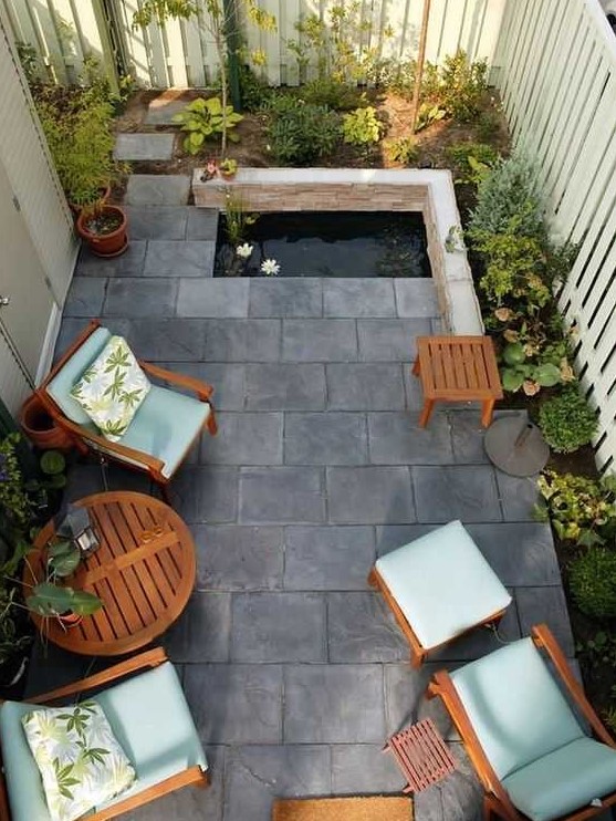 a small and zen like paved patio with tiles on the ground, a tiny pond, some growing plants and cool garden furniture with blue upholstery a small and zen-like paved patio with tiles on the ground, a tiny pond, some growing plants and cool garden furniture with blue upholstery