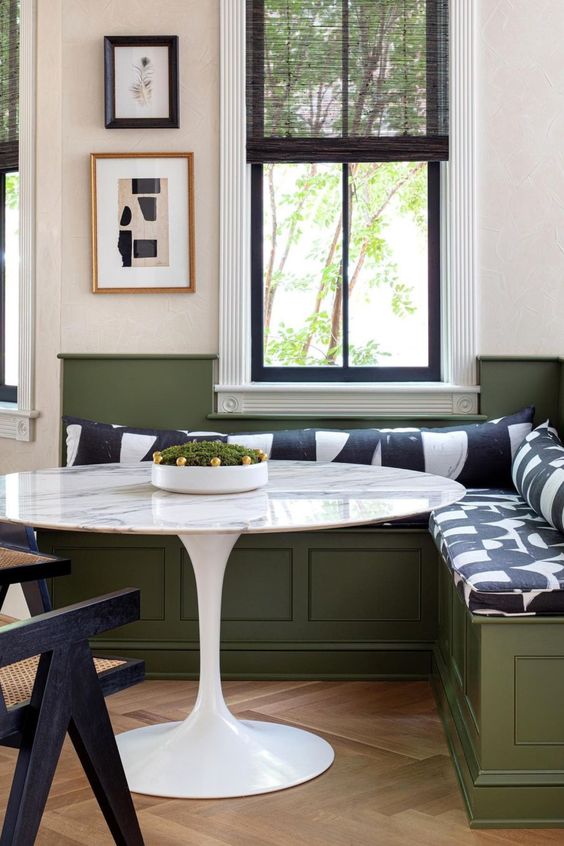a cozy breakfast nook with an olive green corner storage bench, a round table, printed upholstery and some artwork