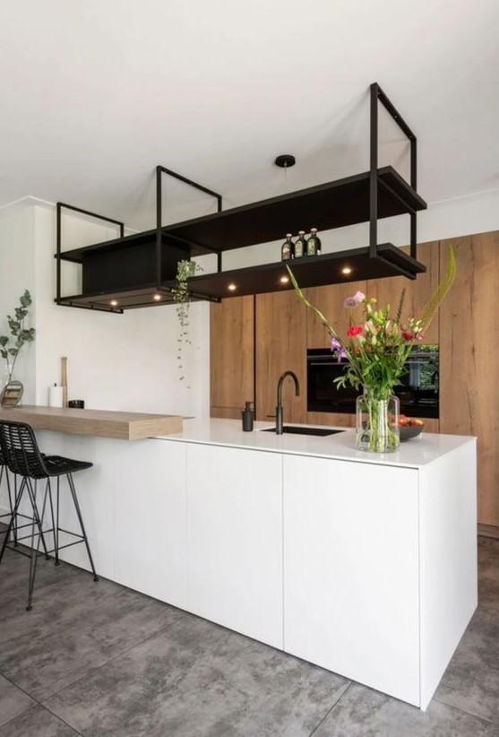 a minimalist kitchen with a large stained storage unit, a sleek white kitchen island, a black suspended shelf and black stools