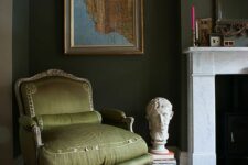 34 a dark green living room with a fireplace, an olive green chair, some art, books and a mirror in an ornated frame