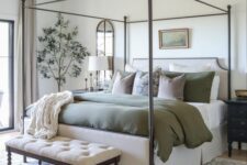 35 a farmhouse bedroom in neutrals, with a metal frame bed and olive green bedding, an upholstered bench, some art and plants