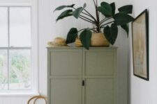 36 a large and pretty olive green wardrobe, potted plants on top, a chair and a frame artwork for a lovely space