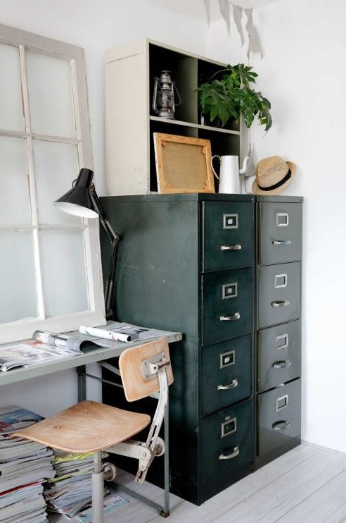 a vintage industrial home office with a metal desk and a plywood chair, a black card cabinet for storage, a table lamp and some greenery