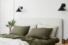 39 a peaceful bedroom done in neutrals, with a creamy upholstered bed, olive green and white bedding, black sconces and rattan nightstands
