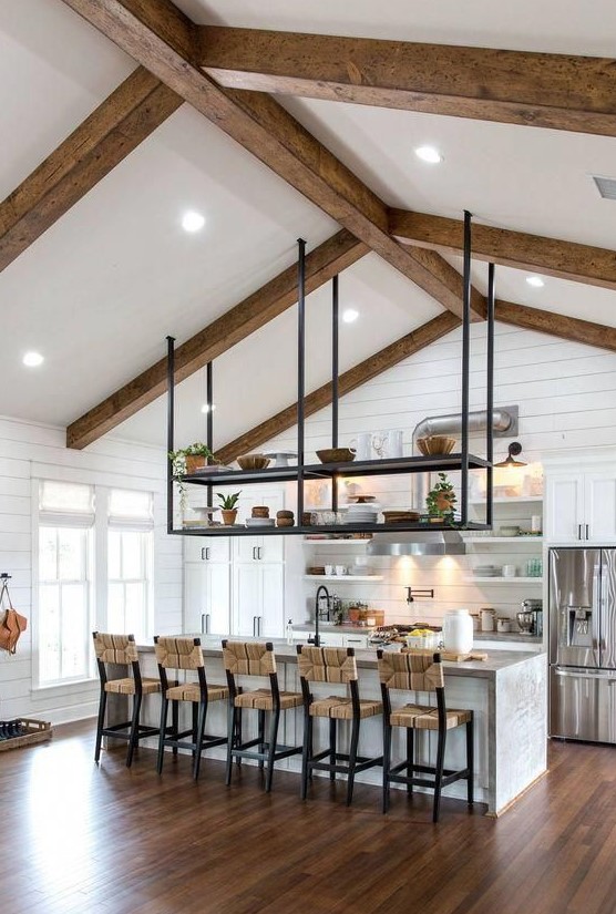 a white cottage kitchen clad with beadboard, with profiled cabinets, a large kitchen island and black suspended shelves over it