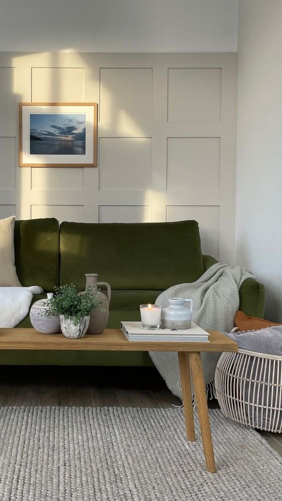a Scandinavian living room with creamy paneling, an olive green sofa and neutral textiles, a wooden bench with decor