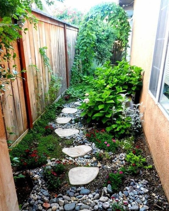 a small and bright side garden nook with pebbles, greenery and bright blooms, shrubs and a climbing plants on the fence a small and bright side garden nook with pebbles, greenery and bright blooms, shrubs and a climbing plants on the fence