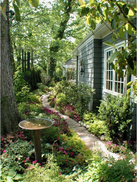 a little and lovely side garden with lots of greenery and blooms, with a stone pathway and a bird bath plus some trees a little and lovely side garden with lots of greenery and blooms, with a stone pathway and a bird bath plus some trees