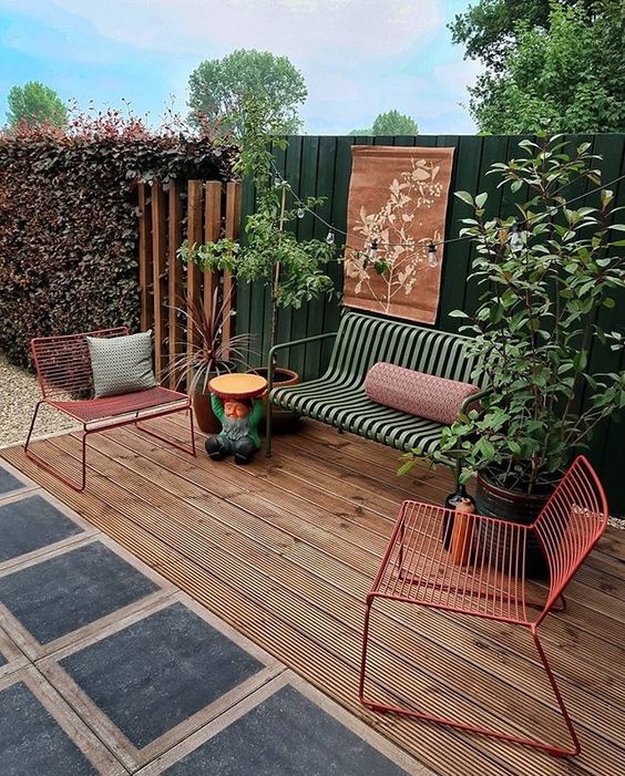 a welcoming deck with pretty and bold metal outdoor furniture, with some potted plants and a dark green fence a welcoming deck with pretty and bold metal outdoor furniture, with some potted plants and a dark green fence
