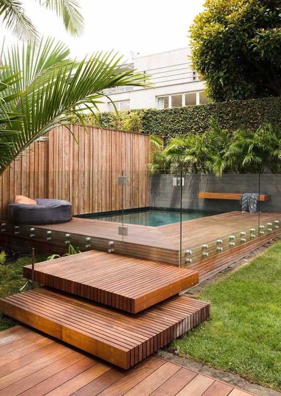 a tropical outdoor space with greenery, a rich stained deck and steps and a small pool with a bench and a pouf a tropical outdoor space with greenery, a rich-stained deck and steps and a small pool with a bench and a pouf