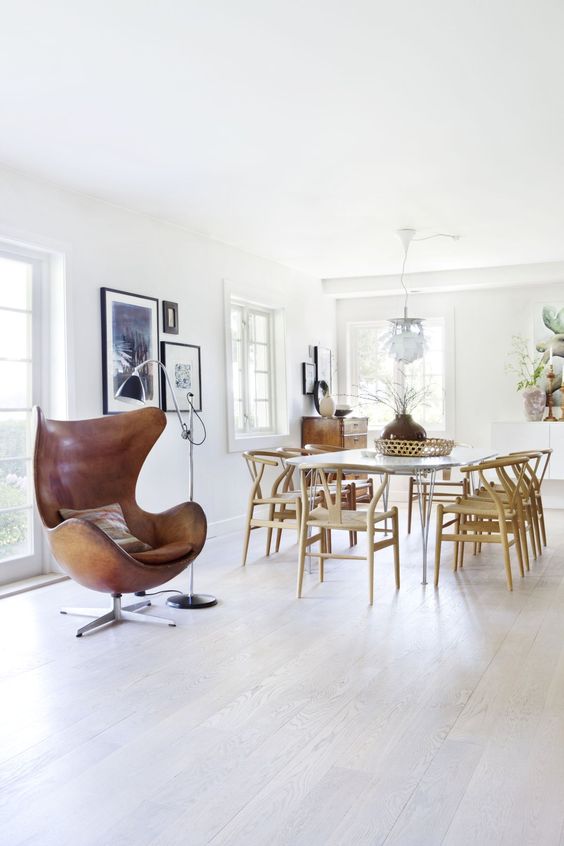 a Scandinavian dining space with a hairpin leg table and Wishbone chairs, a brown leather Egg chair, a floor lamp and some art